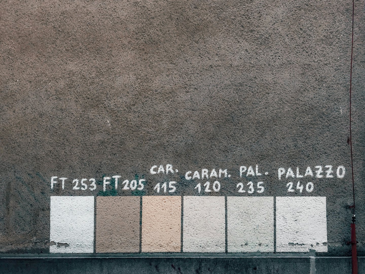 Campioni di vernice rettangolari con etichette numeriche su un muro di stucco.