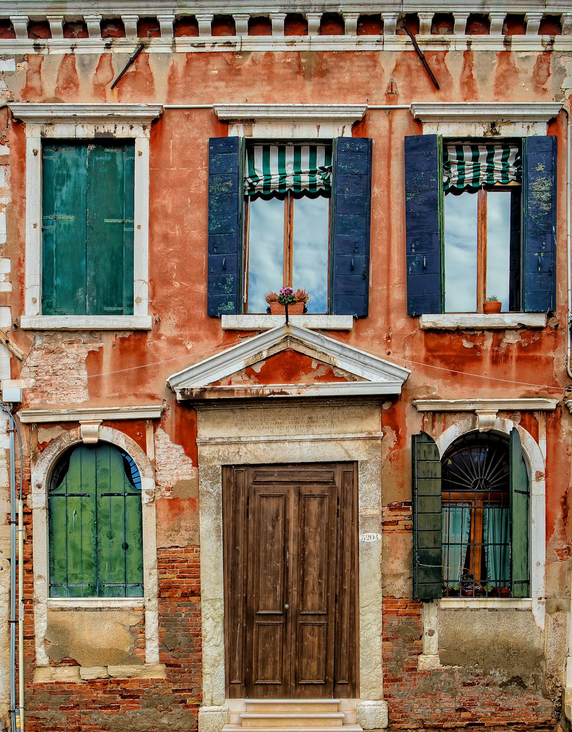 Facciata di un edificio invecchiato con vernice scrostata e persiane in legno colorate.