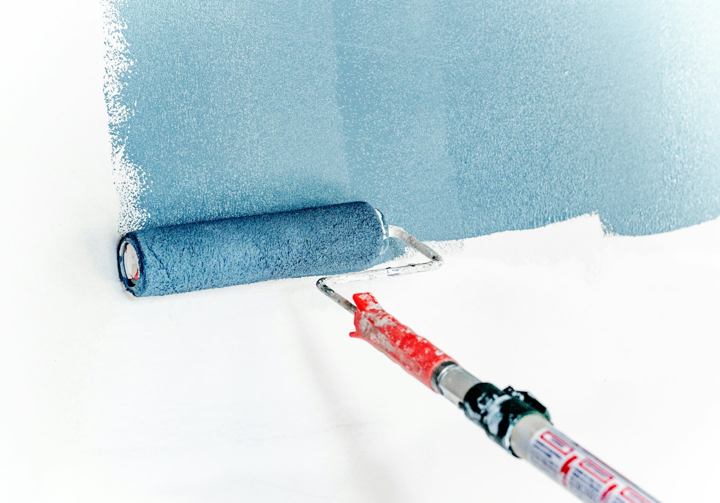 Rullo da pittura che applica vernice azzurra a una parete bianca.