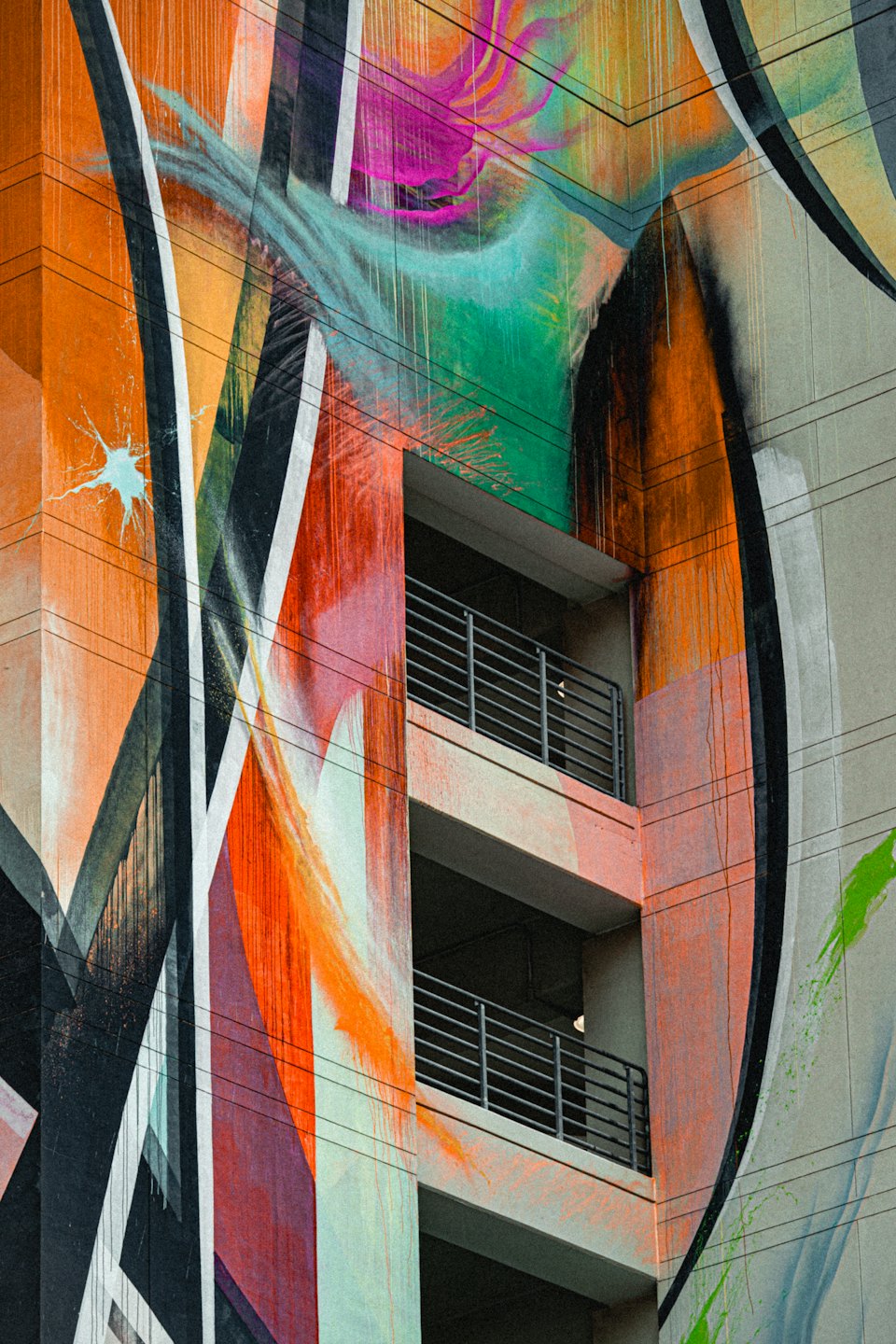Facciata di un edificio moderno con un murale astratto dai vivaci colori arancione e verde.